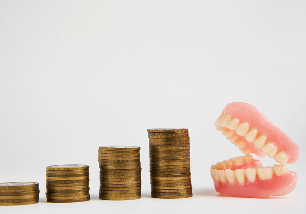 Stacked coins beside dentures showing the Dentures Cost
