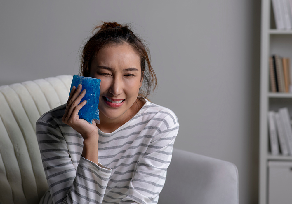 Woman applying ice pack for tooth pain needing Emergency Dentist